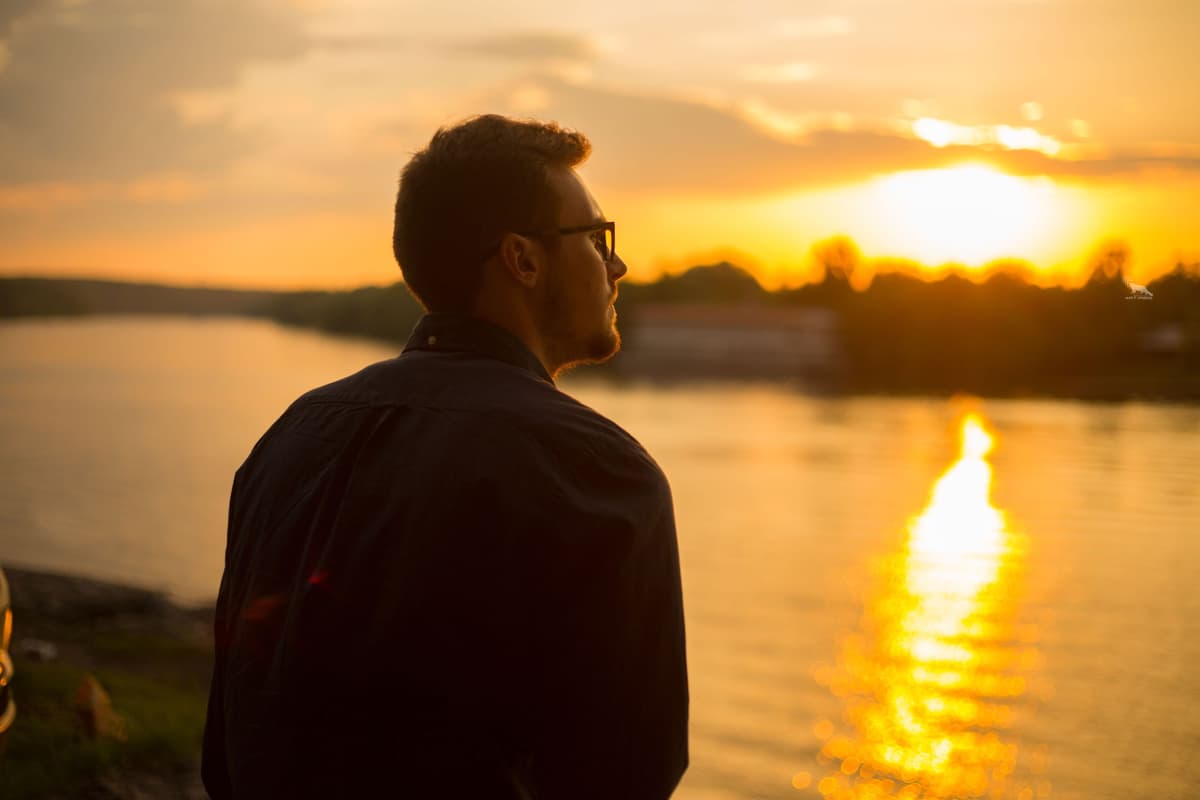 Homem contemplando o pôr do sol sobre a água